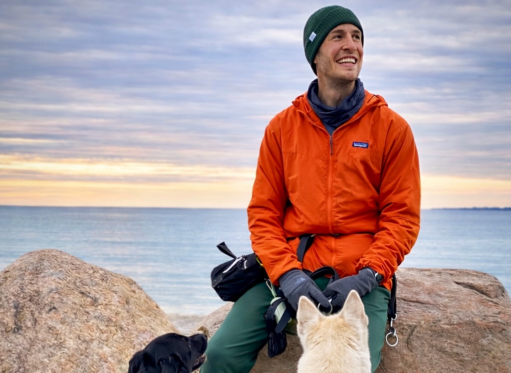 Tom sitting on shoreline rocks with two dogs in southeastern Connecticut